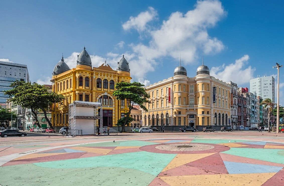 Vista da Praça do Marco Zero, no Recife Antigo, com edifícios históricos e céu azul.